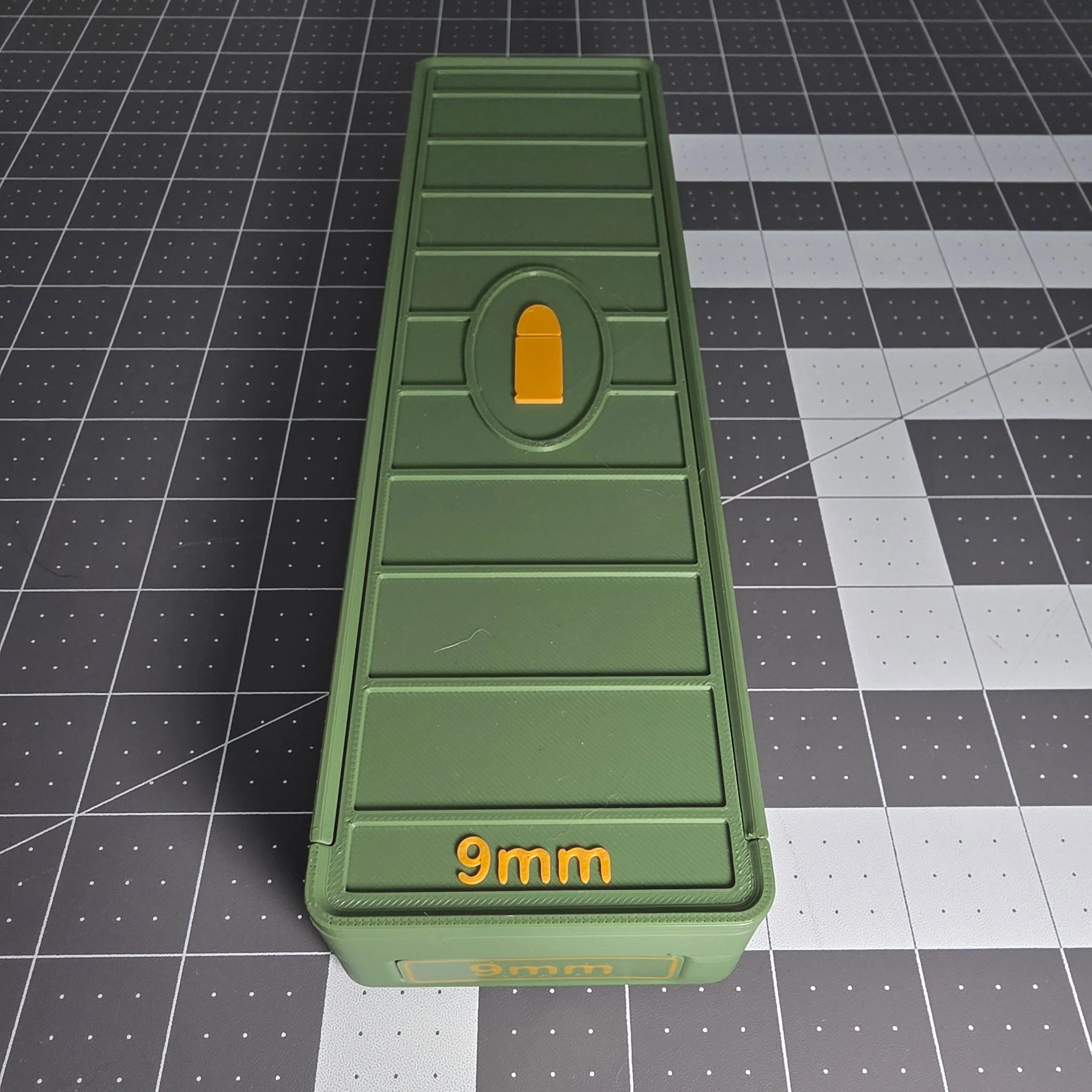Green 3D-printed 9mm ammo storage box with yellow latch on a grid cutting mat.