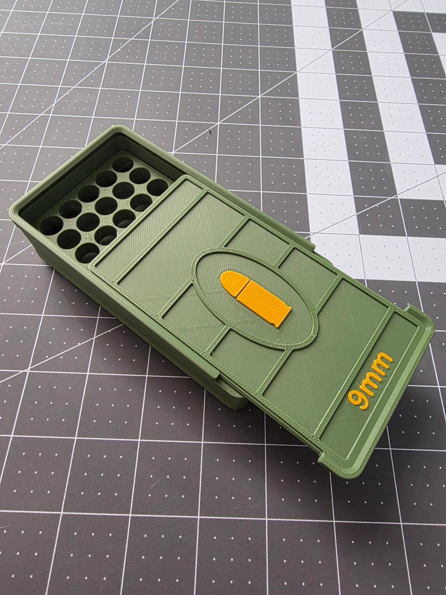Olive green 3D-printed 9mm ammo storage box with yellow bullet design on a grid mat
