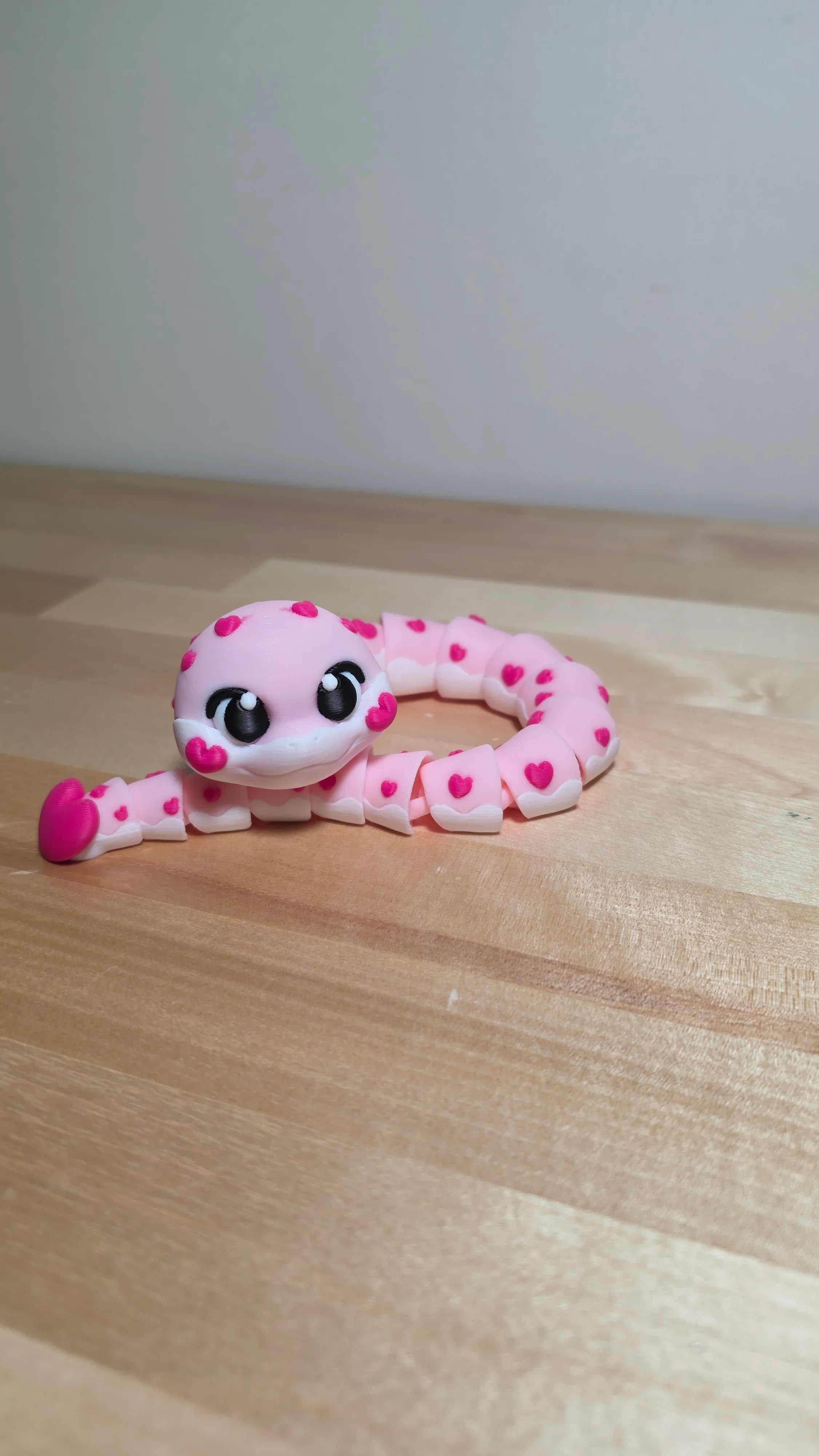 Pink 3D-printed articulated gecko toy with heart designs on a wooden surface