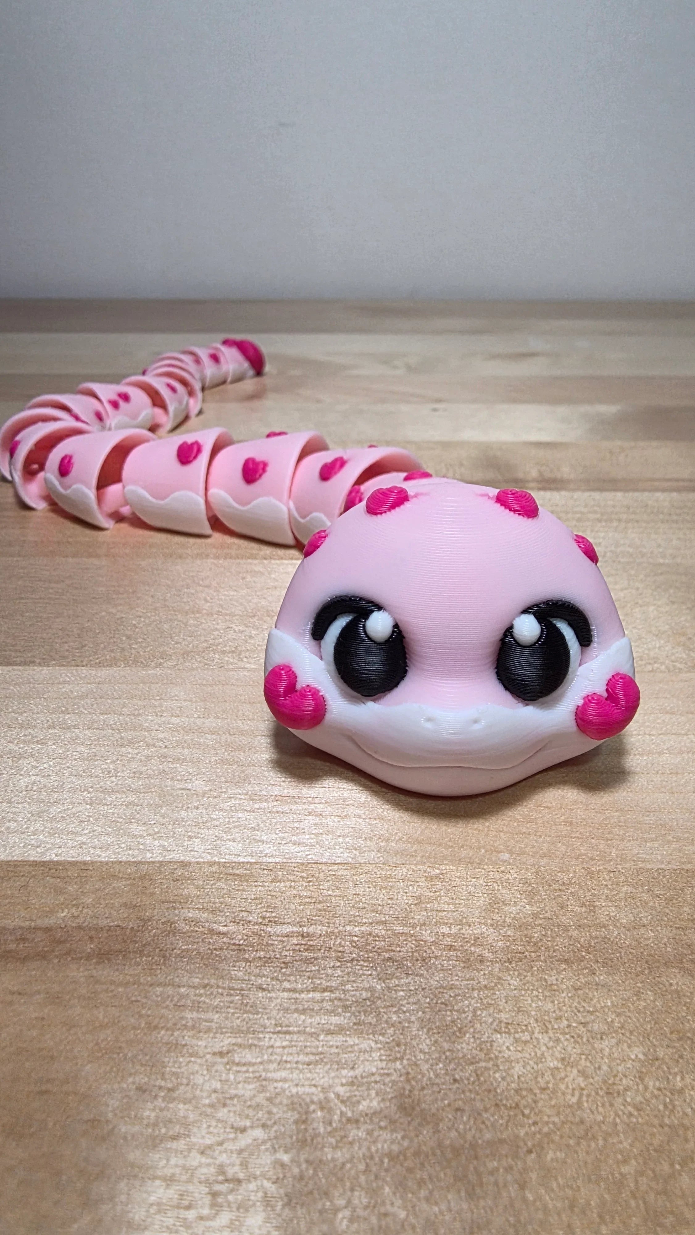 3D-printed pink articulated snake toy with heart accents on a wooden surface