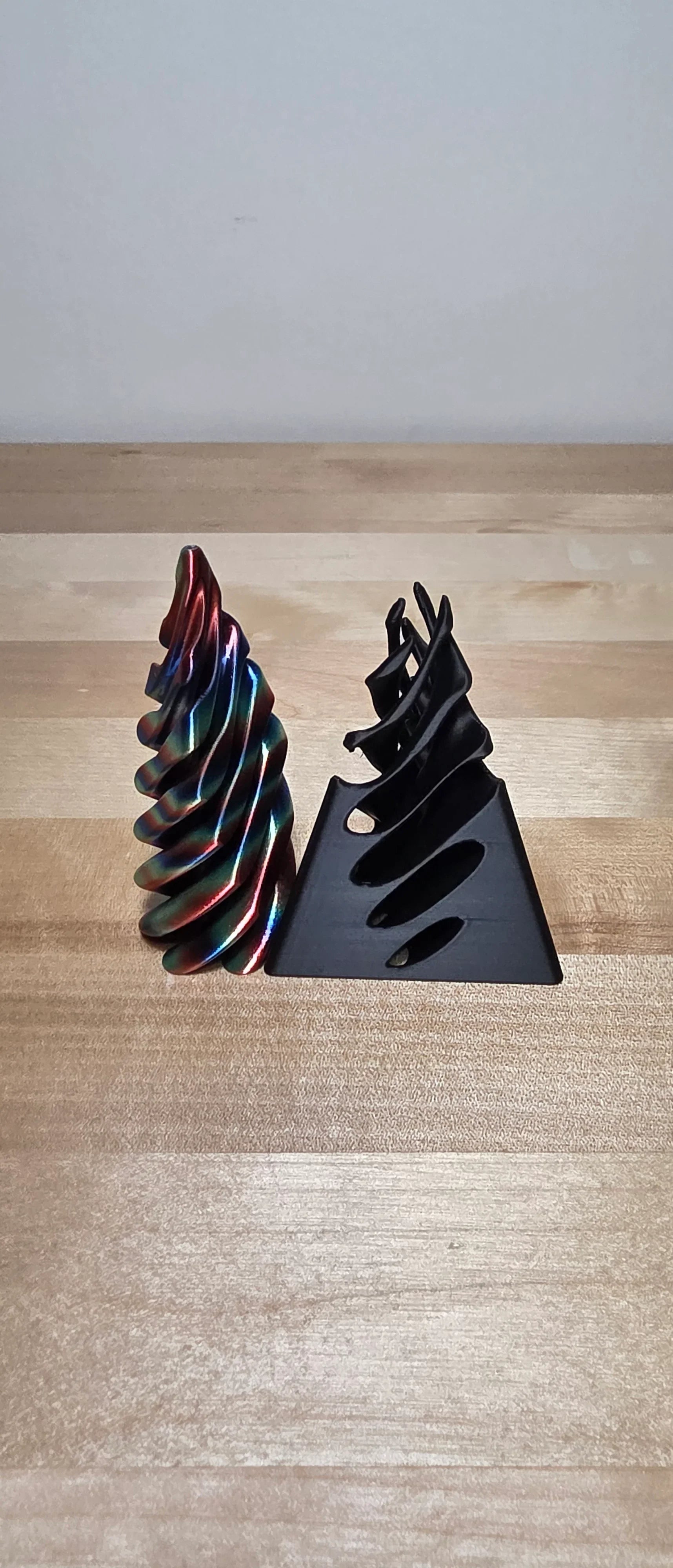 Two 3D printed spiral sculptures, one rainbow and one black, on a wooden table