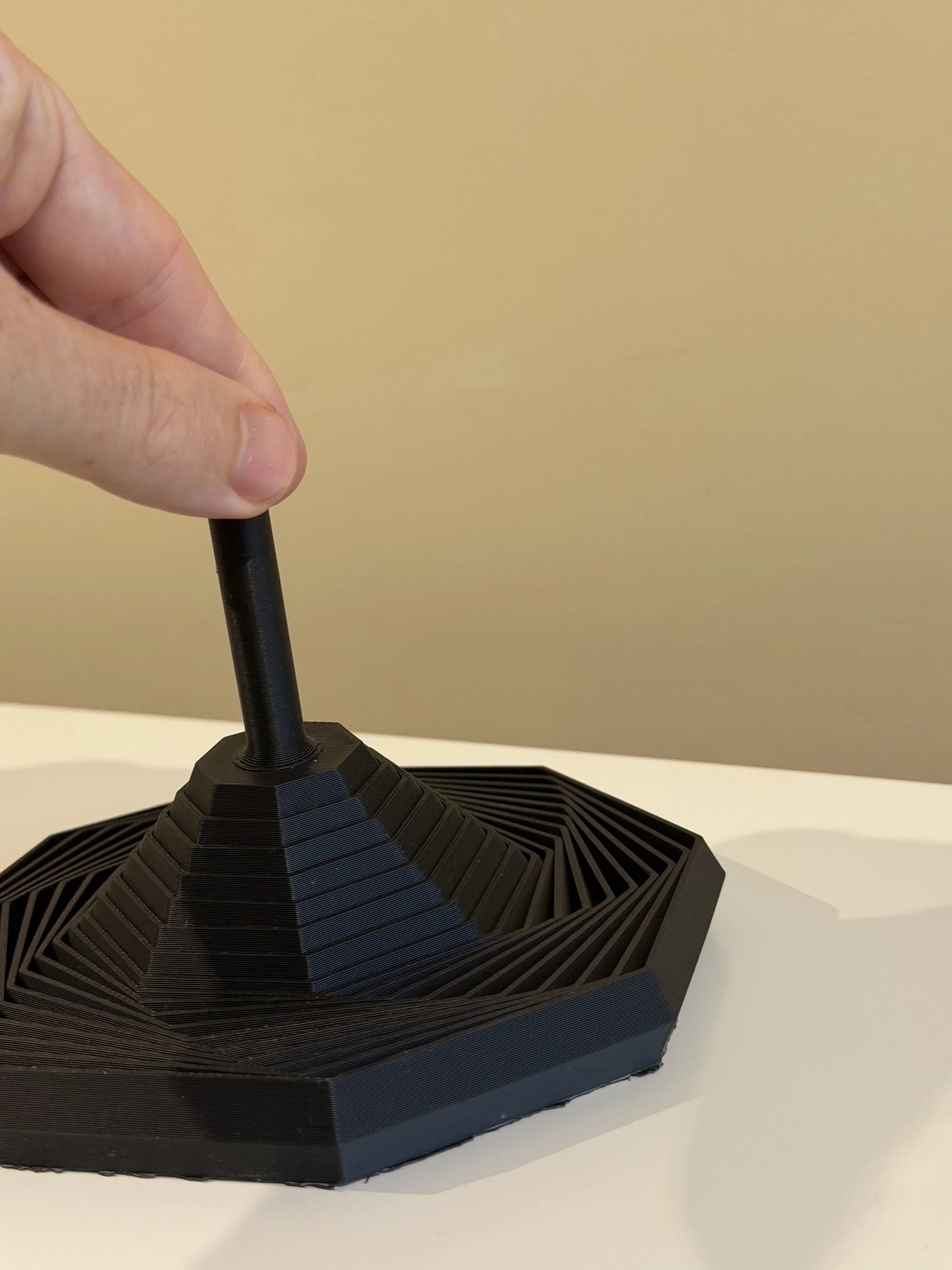 Hand holding black 3D-printed geometric storage organizer on white table