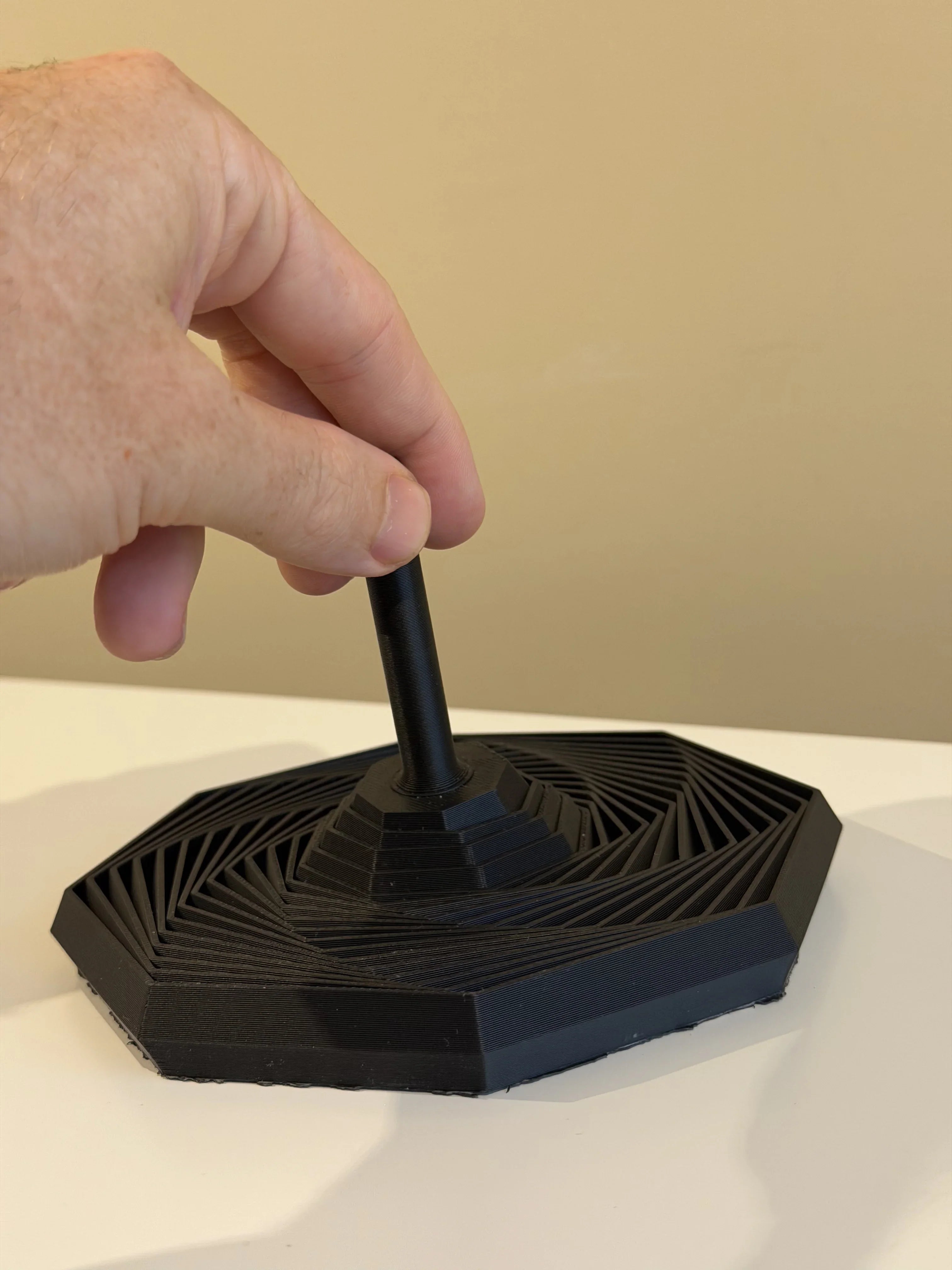 Hand holding a black 3D-printed geometric stand on a white surface